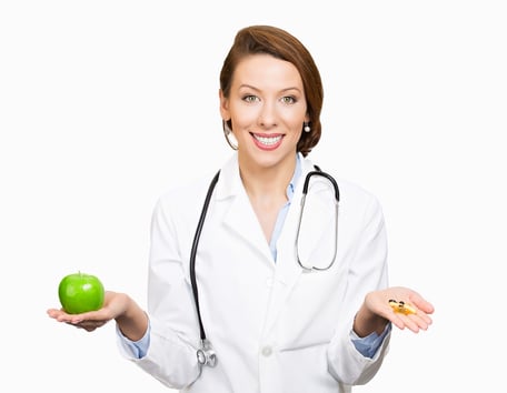 Closeup portrait smiling, female health care professional, family doctor, endocrinologist,  nutritionist holding green apple, pills, vitamins. Diet modification, diabetes management, drugs alternative