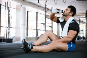 Fitness man wearing blue shorts and black t-shirt sitting on the floor and drinking water