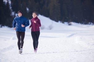 healthy young couple jogging outside on snow in forest. athlete running on  beautiful sunny winter day