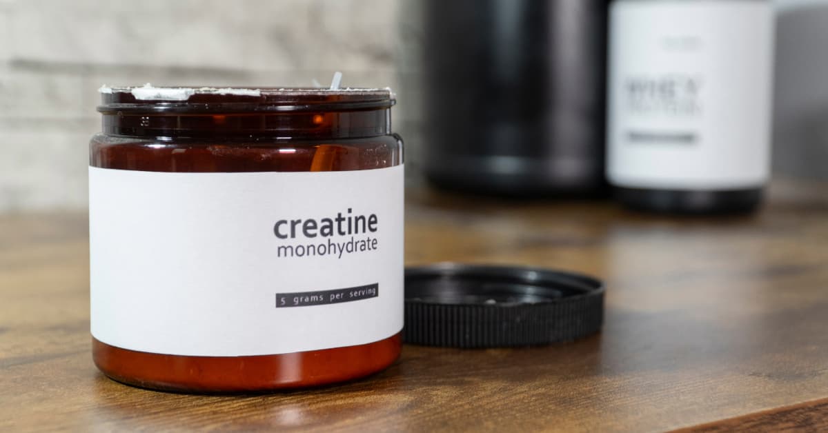 a jar of creatine powder sitting on a wooden countertop with the lid off ready to be taken