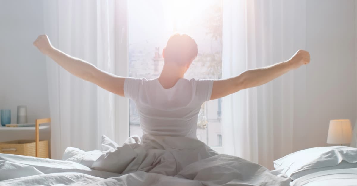 young, fit man in a white t-shirt waking up in bed to the sunrise