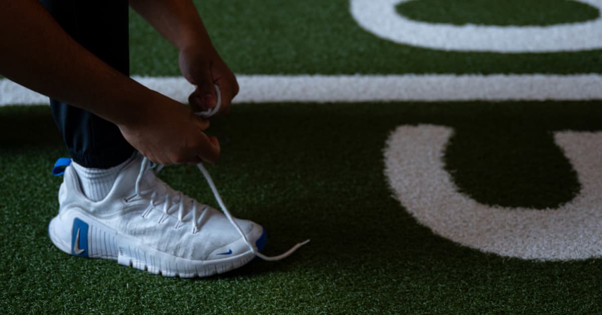 A man tying his shoelace in the gym on the turf before a bodyweight workout 
