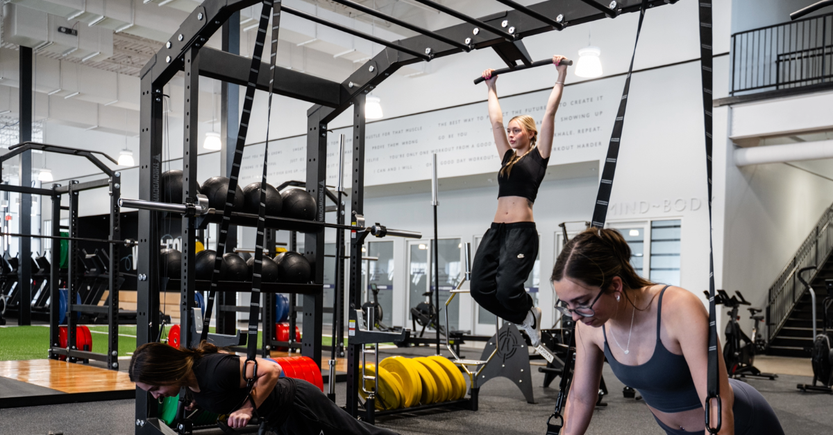 One woman preforming hanging knee raises and two other women on TRX straps inside o2 fitness clubs