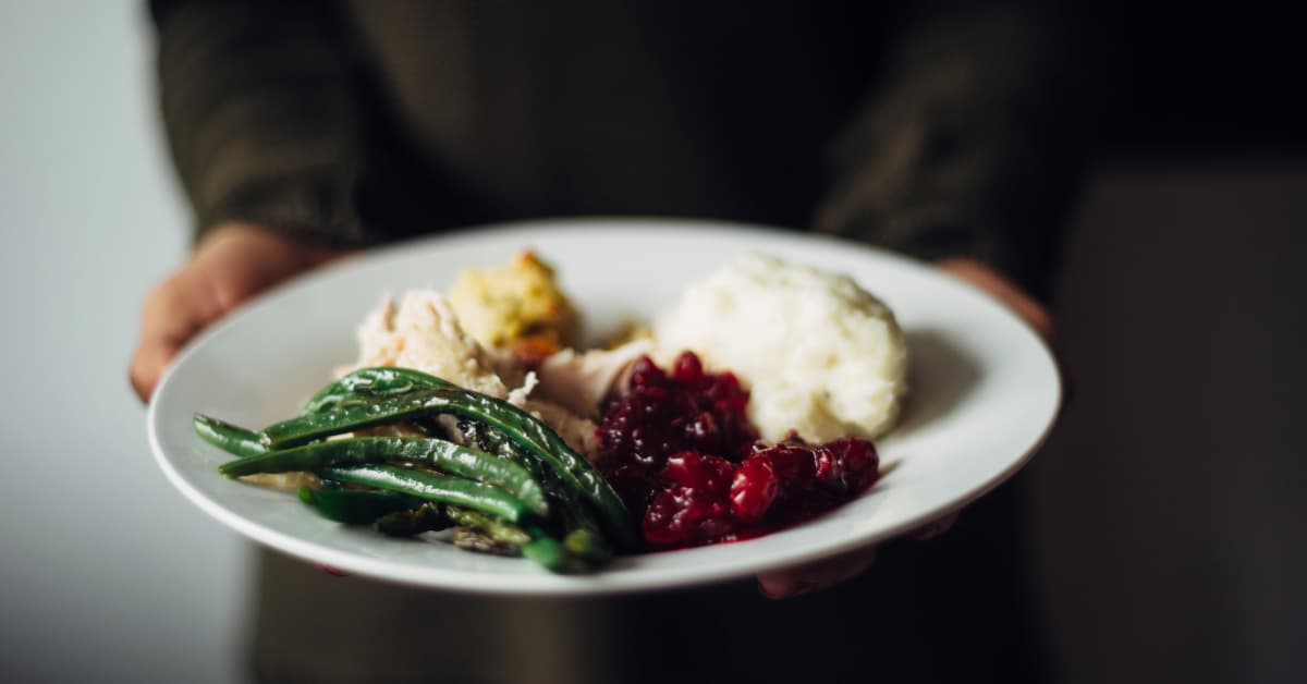 a person holding a plate full of traditional thanksgiving foods 