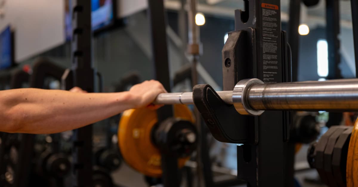 man holding onto a steel barbell racked in a squat rack inside o2 fitness clubs