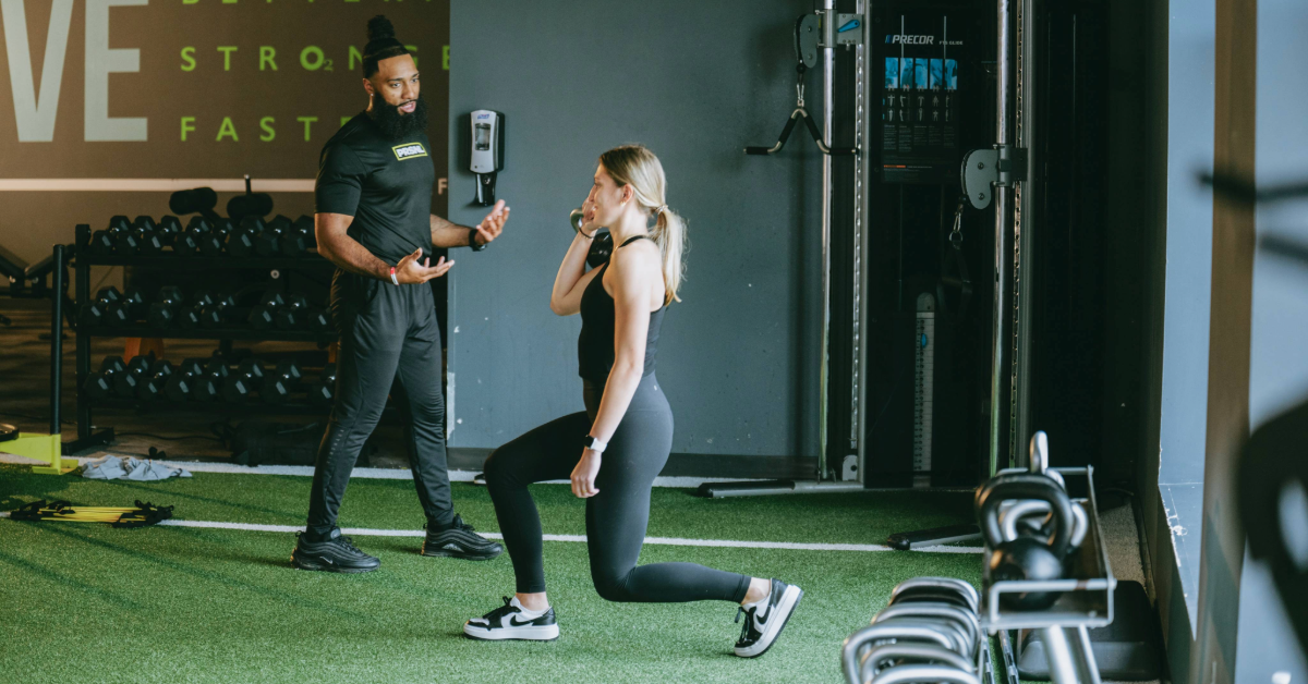 woman in a black workout set doing a leg day while being coached by a personal trainer at o2 fitness clubs durham location