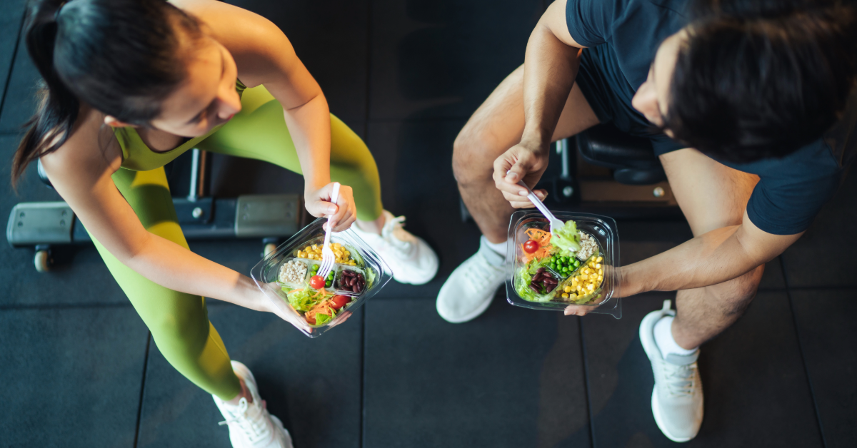 man and a woman eating a salad in the gym talking to each other