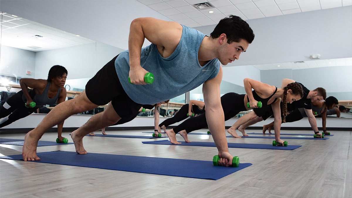 class at O2 Fitness Clubs holding a plank with weights on a yoga mat for strength 