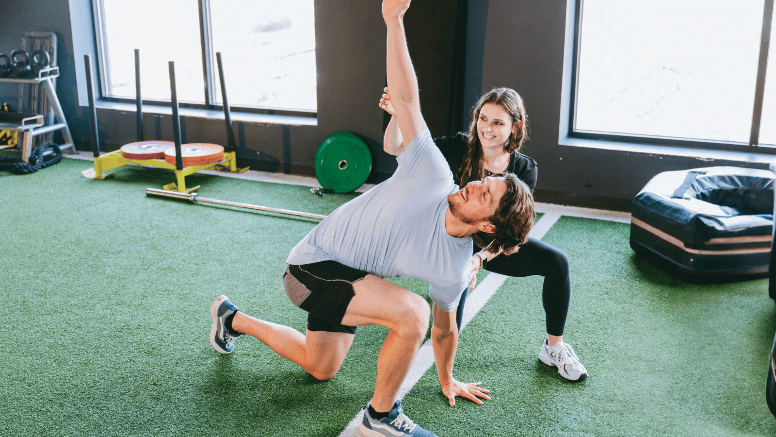 man stretching on turf in gym with female personal trainer