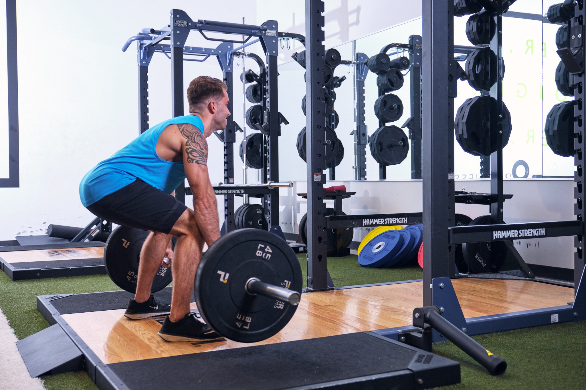 man in a blue tank top and black athletic shorts preparing do deadlift a standard barbell at an O2 fitness clubs